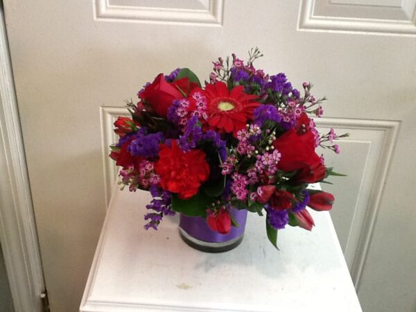 A purple vase with red and pink flowers on top of a table.
