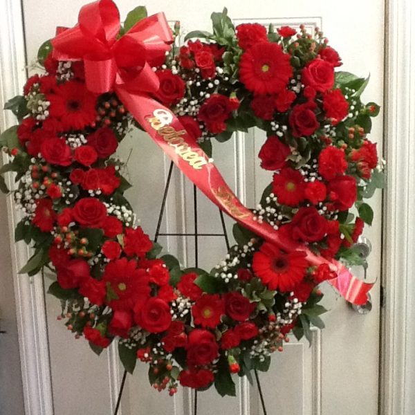 A heart shaped wreath of red roses with a ribbon.