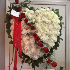 A heart shaped wreath of white flowers and red roses.